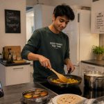 Young Indian student cooking a simple meal in a clean German shared kitchen, looking relaxed and comfortable